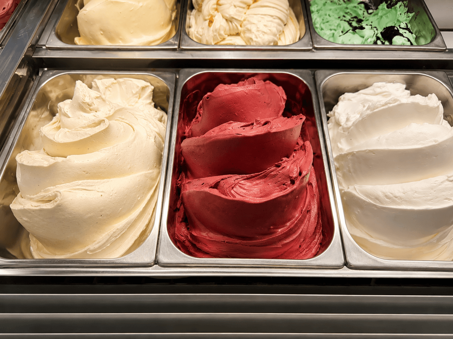 Cremiges Speiseeis in Metallbehältern, kunstvoll aufgetürmt in den Farben Vanille, dunkles Rot und Weiß.
